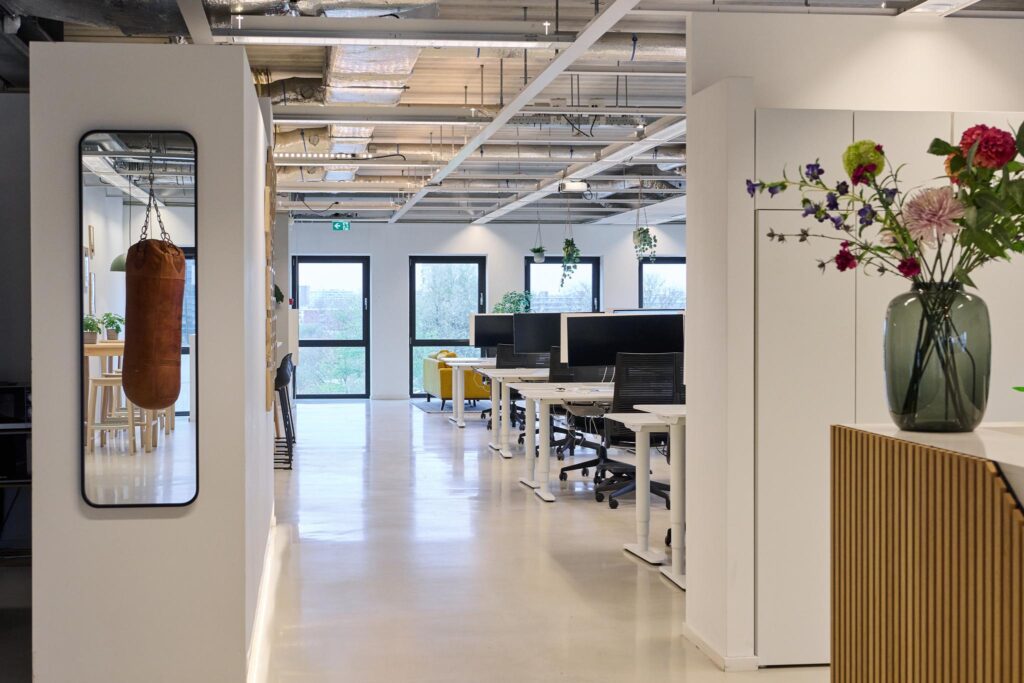 Modern kantoorinterieur aan het John M. Keynesplein met flexwerkplekken, planten, een bokszak en een vaas met bloemen.